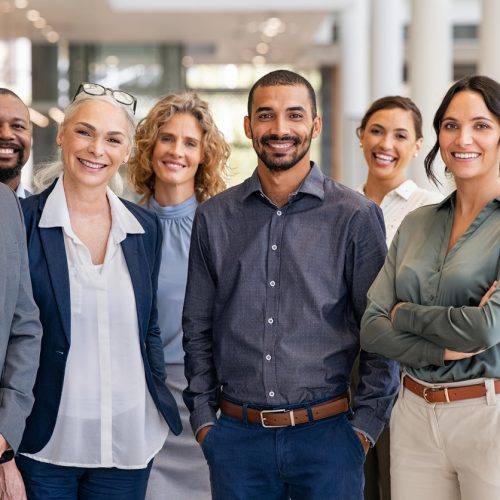 Portrait of successful group of business people at modern office looking at camera. Portrait of happy businessmen and satisfied businesswomen standing as a team. Multiethnic group of people smiling and looking at camera.